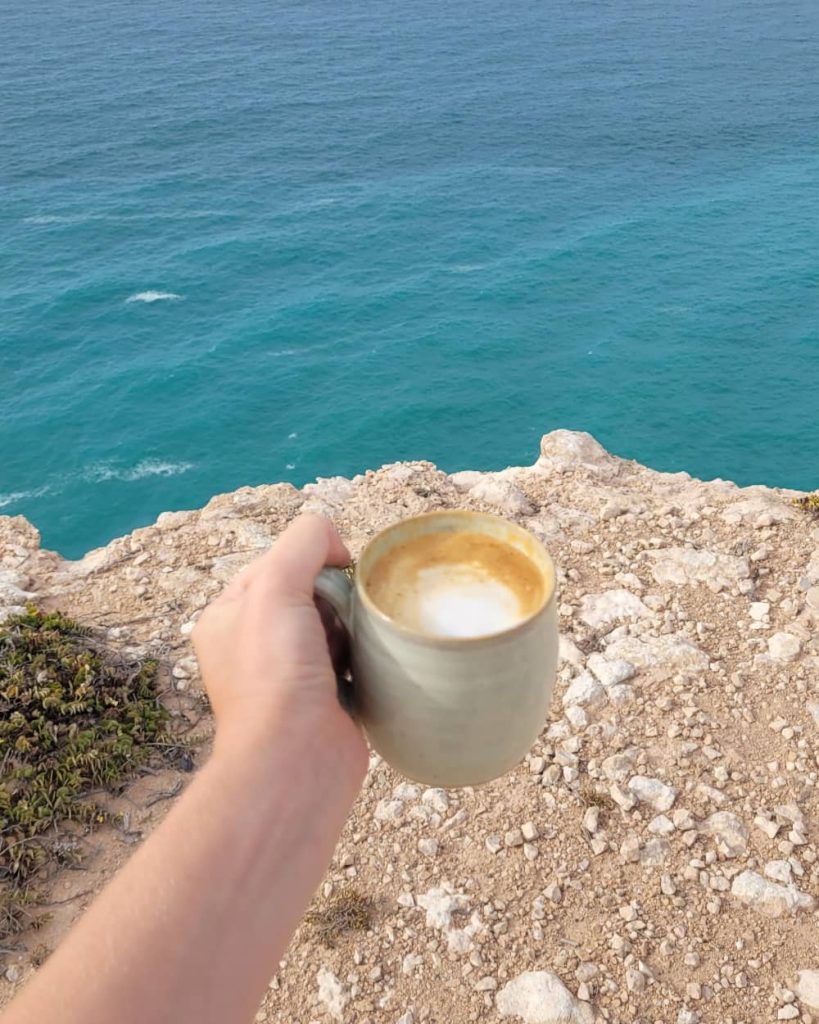 Woman holding a cup of coffee near the edge of the Bunda Cliffs, in Australia. Part of any Nullarbor road trip