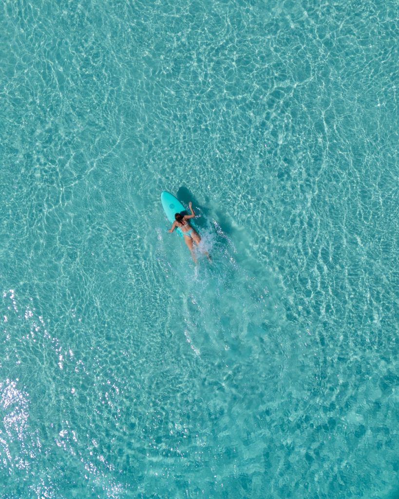 Someone paddling on top of a surf board in the turquoise waters of Esperance, Western Australia