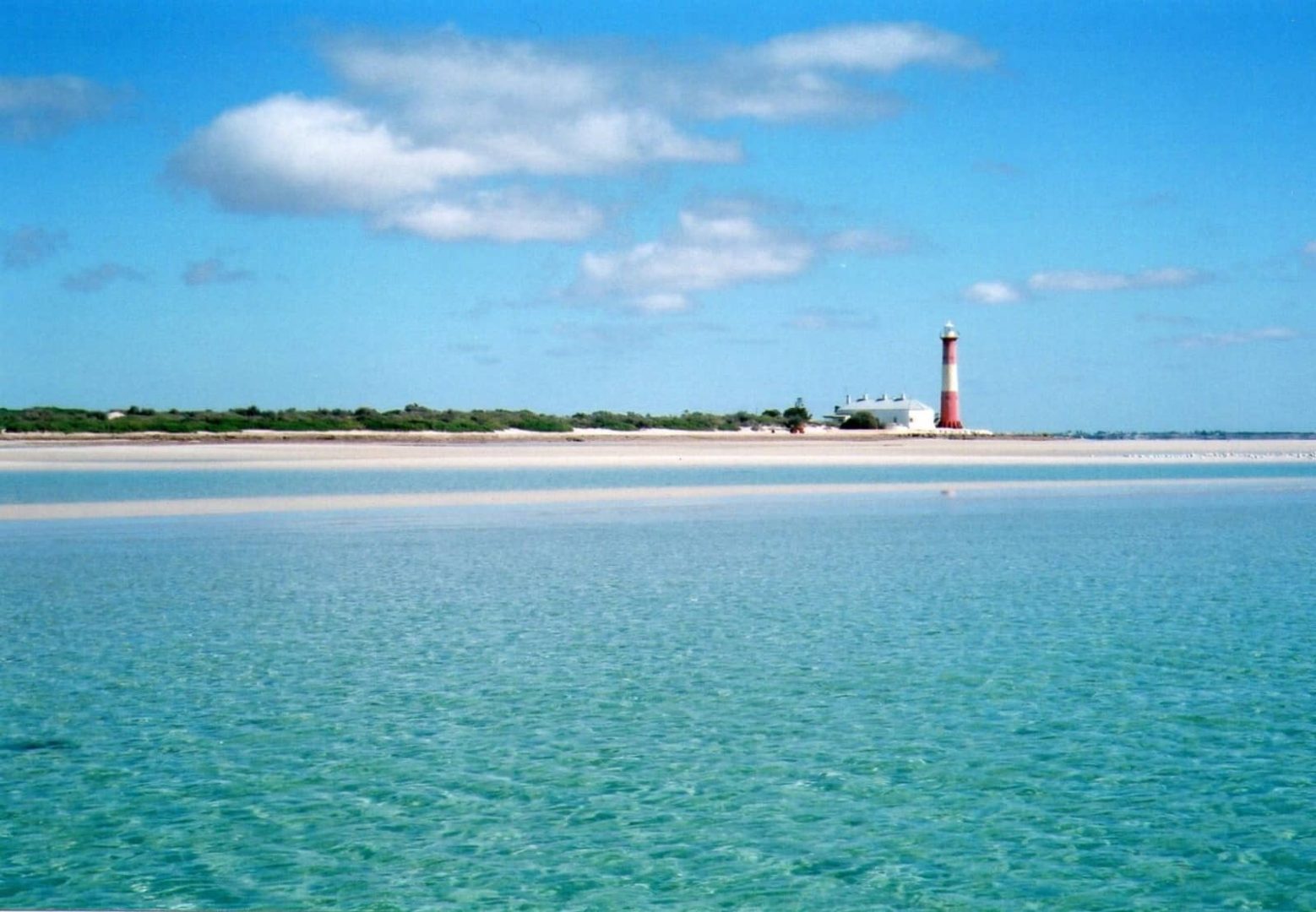 Crystal clear shallow water with a view of the red-and-white Troubridge Island lighthouse in the distance, seen during a Yorke Peninsula road trip.