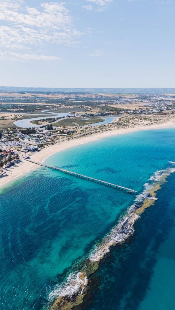 Aerial shot of the long jetty and clear turquoise water at Port Noarlunga, with reef visible below the surface on a Melbourne to Perth road trip stop.