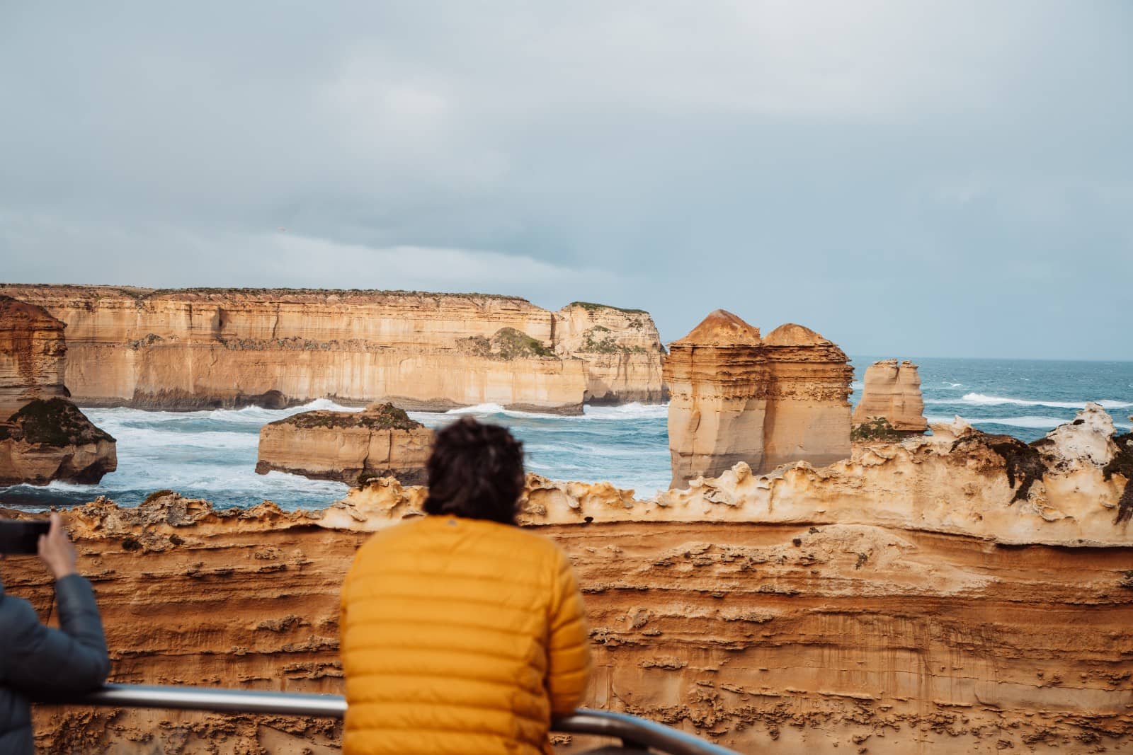 Two people viewing the iconic limestone stacks of the Razorback on the Great Ocean Road, a scenic coastal detour on a Melbourne to Darwin road trip.
