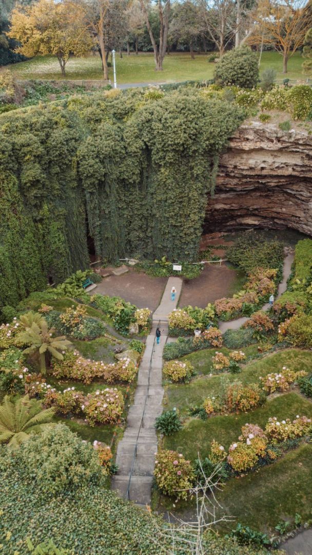 A sunken garden surrounded by cliffs and covered in hanging vines and flower beds at Umpherston Sinkhole in Mount Gambier, a stop on the Melbourne to Darwin road trip.