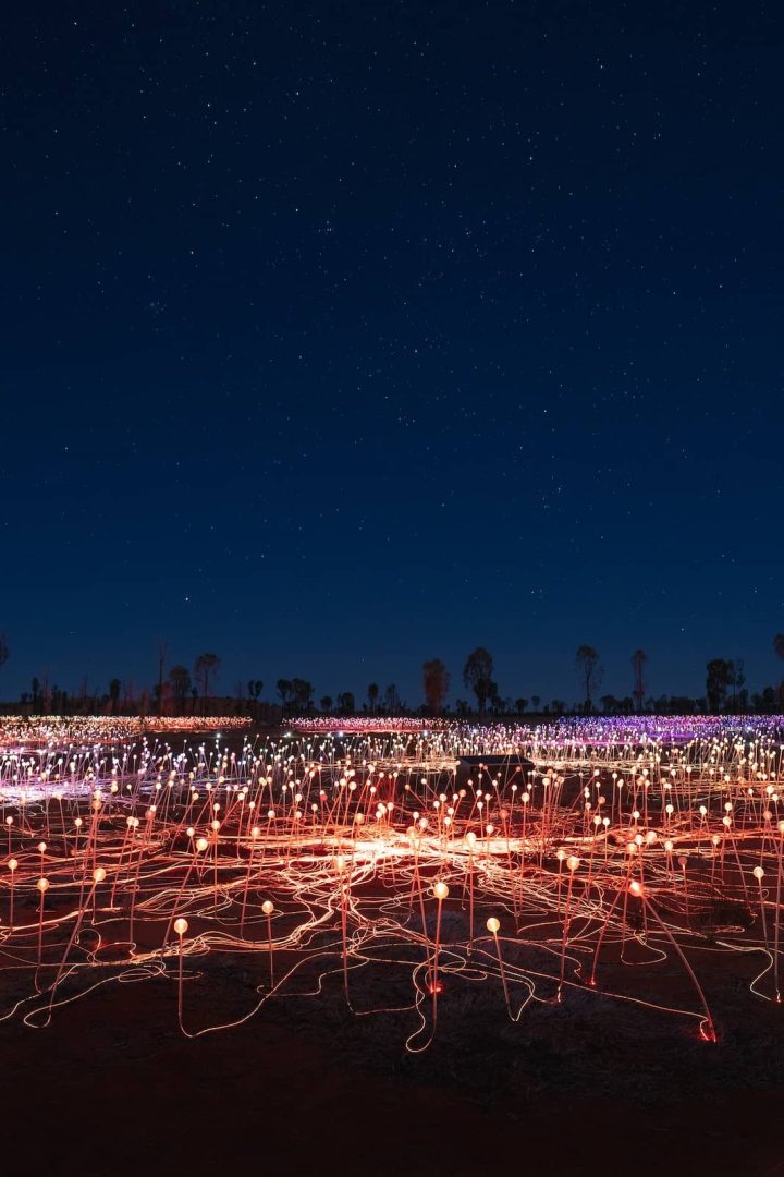 Bruce Munroโs Field of Light installation glows under a starry night sky near Uluru, a popular stop on the red centre way. Thousands of coloured lights spread across the desert floor in vibrant patterns.