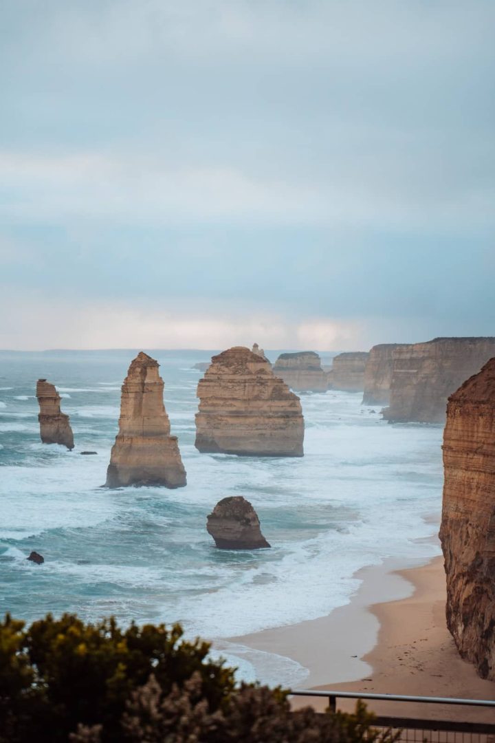 The Twelve Apostles limestone stacks rise out of the ocean under overcast skies, seen from a coastal lookout on the Great Ocean Road during a Melbourne to Perth road trip.