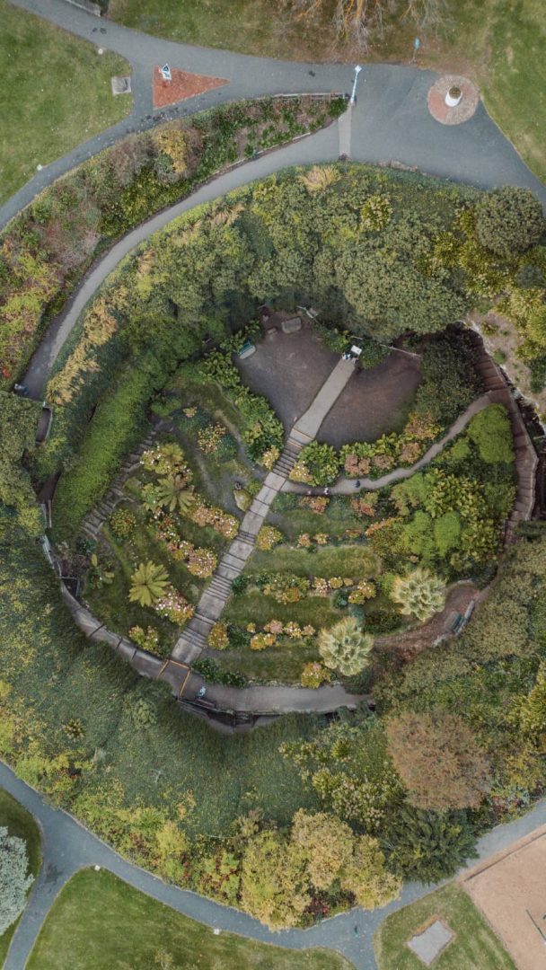 Aerial view of the circular Umpherston Sinkhole garden in Mount Gambier, showing paths, terraces and dense vegetation on a Melbourne to Perth road trip route.