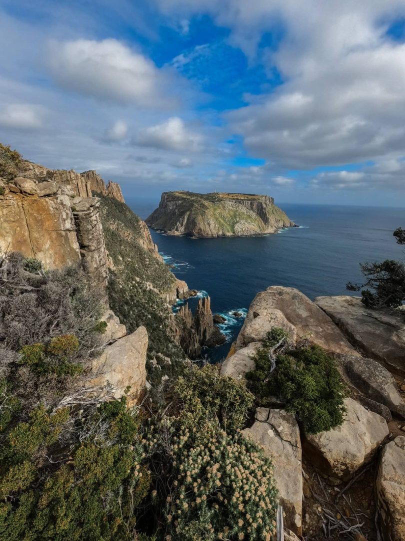 Coastal cliffs and Tasman Island in the distance under a patchy blue sky, viewed from a high lookout on the Three Capes Track for free.