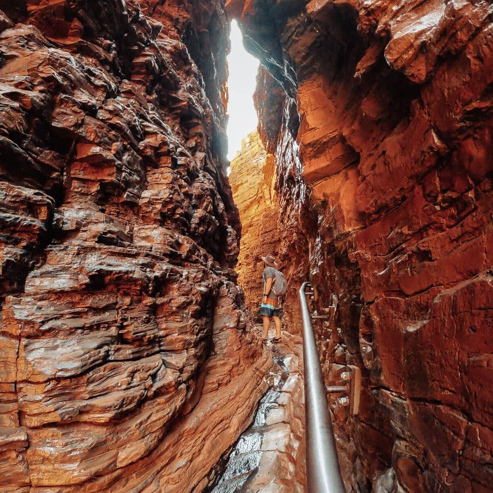 Man walking along path amongst rocks next to a handrail. Widely considered one of the top ten best things in Karijini. This is the Handrail Pool in Karijini.