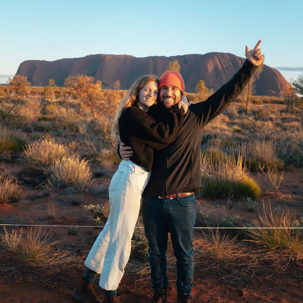 A man and woman hugging in front of Uluru at sunrise. This is one of the perfect times to see Uluru. This is Uluru in the Northern Territory. 