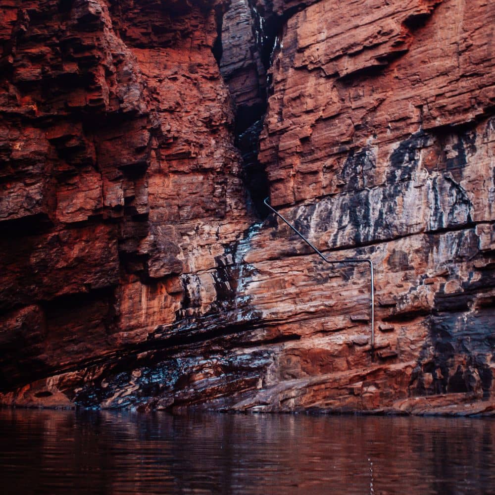 A handrail leading down to a body of water, surrounded by red rocks. One of the many spots to see at the Handrail pool in Weano gorge.