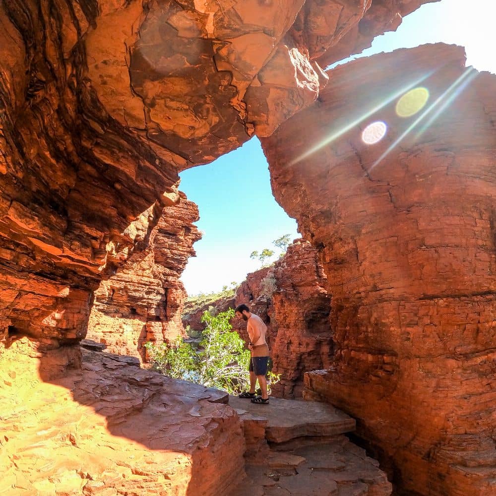 Man walking through gorge while looking at gorgeous red rocks surrounding him. Many travellers consider it one of the best sites in Karijini. This is Kalamina Gorge in Karijini.