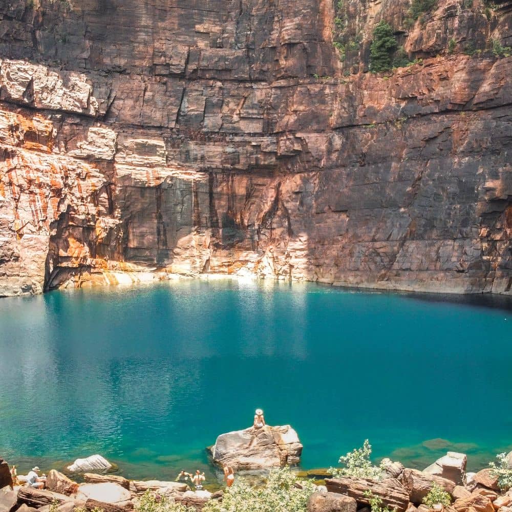 A woman sitting on a rock looking out at a vast expanse of water surrounded by rock formations. One of the stops at some of the Northern Territories best hiking trails. Located in Kakadu National Park in the Northern Territory. 