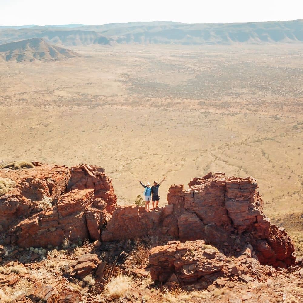 A man and woman standing on the top of a mountain with hands in air. This site is one of the top ten sites in Karijini. Can be found at the top of Mount Bruce in Western Australia's Karijini.
