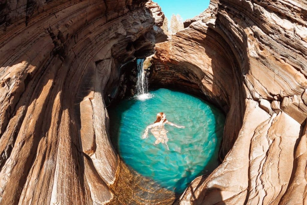 Women swimming in a small rock pool with a small waterfall. This is one of the best things to do in Karijini.