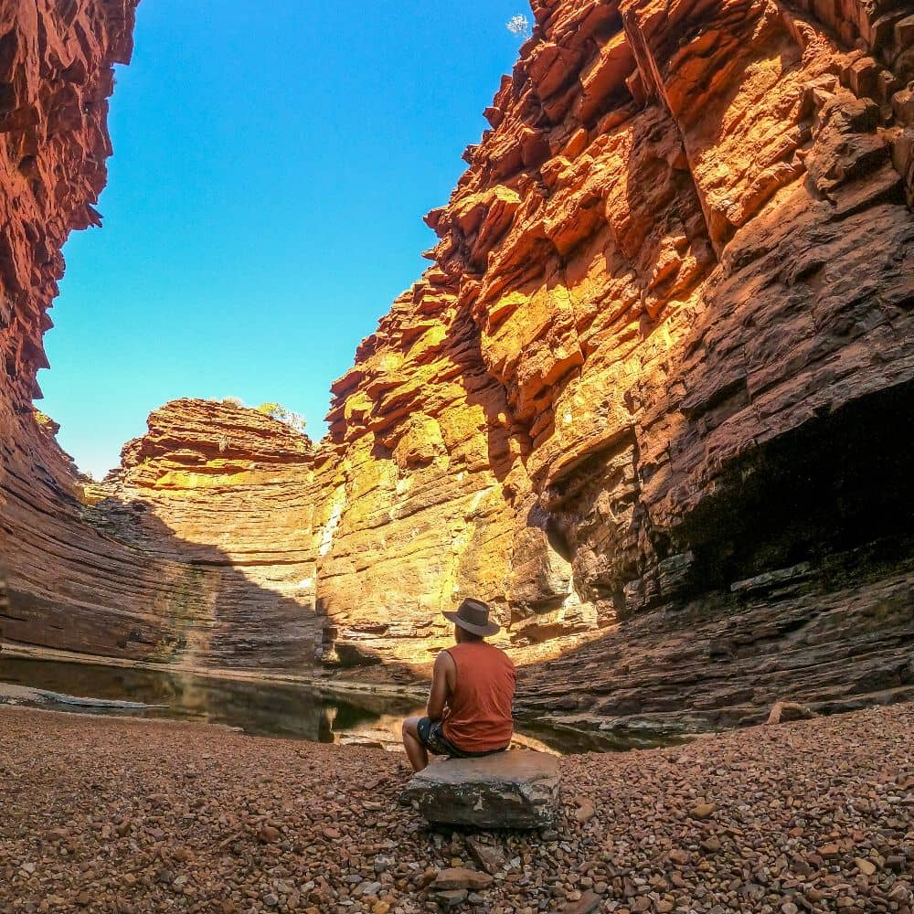 Man sitting on a small rock while overlooking Joffre gorge at the golden hour. Everything can be found at Joffre gorge, including a pool. This is the popular Joffre Gorge in Karijini.