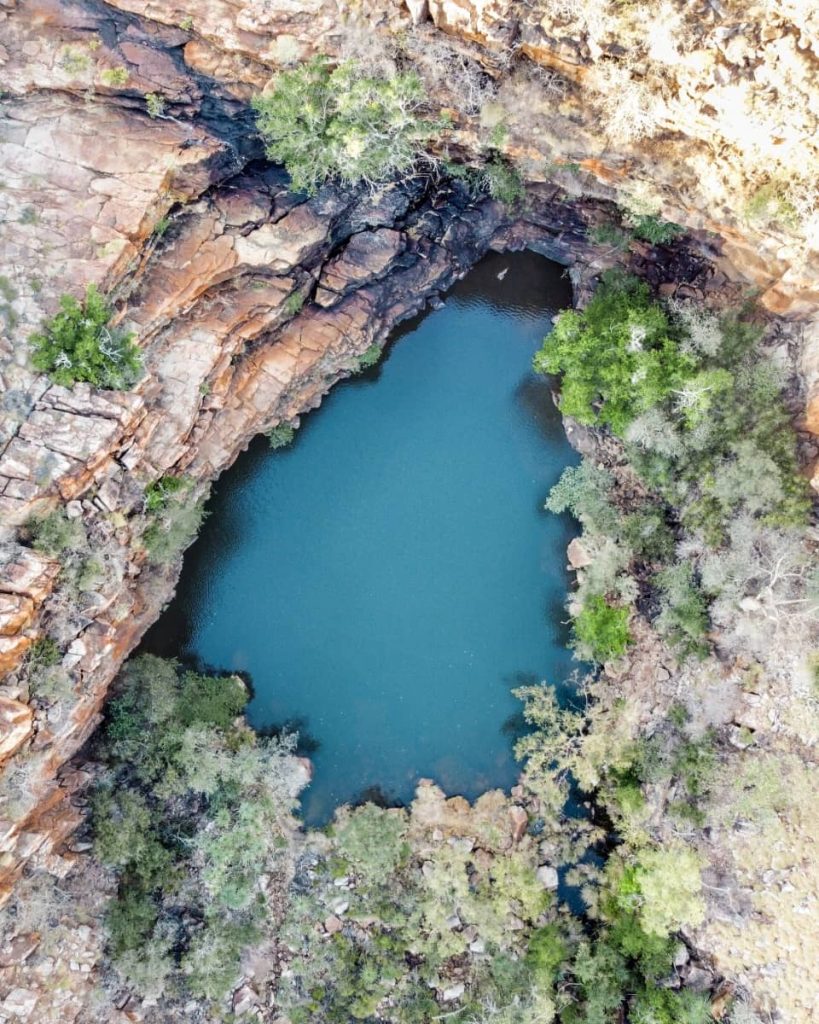 Aerial view of the deep blue waterhole at Galvans Gorge, surrounded by rugged red rock formations and pockets of greenery—one of the scenic and accessible gorges included in many gibb river road itinerary stops.