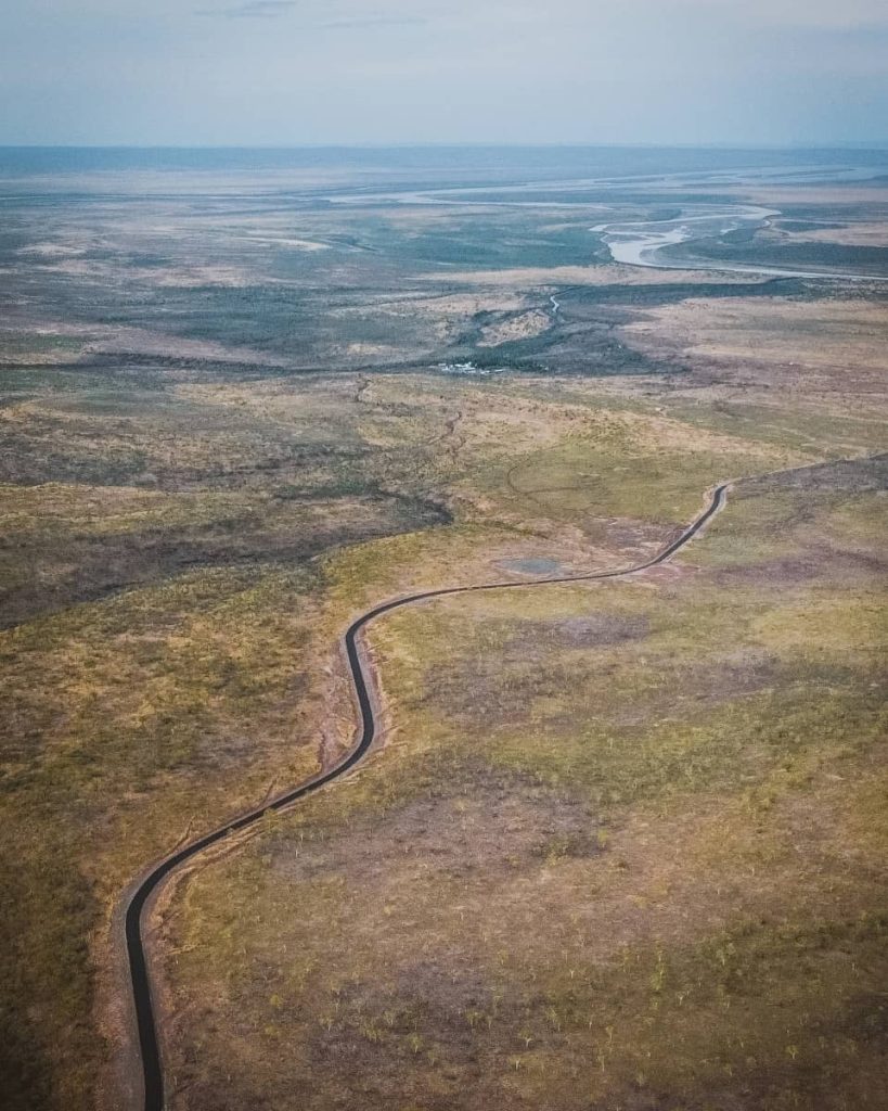 Aerial view of a winding blacktop road cutting through the vast Kimberley plains, with river bends visible in the distance—an expansive landscape often featured in a gibb river road itinerary.