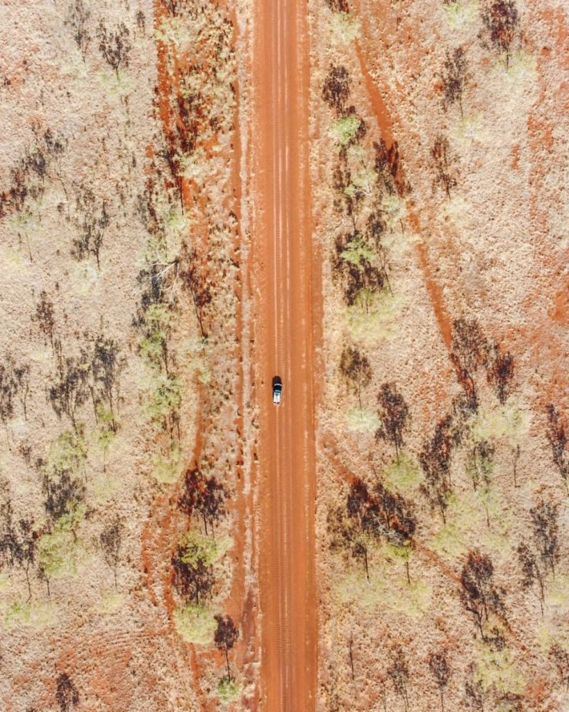 Top-down aerial view of a 4WD driving along a long, straight red dirt track cutting through dry Kimberley bushland—an iconic sight for anyone planning a gibb river road itinerary in Western Australia.