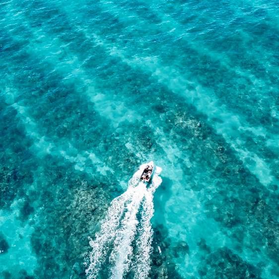An aerial view of a small boat speeding through the vibrant turquoise waters near Exmouth, Western Australia.