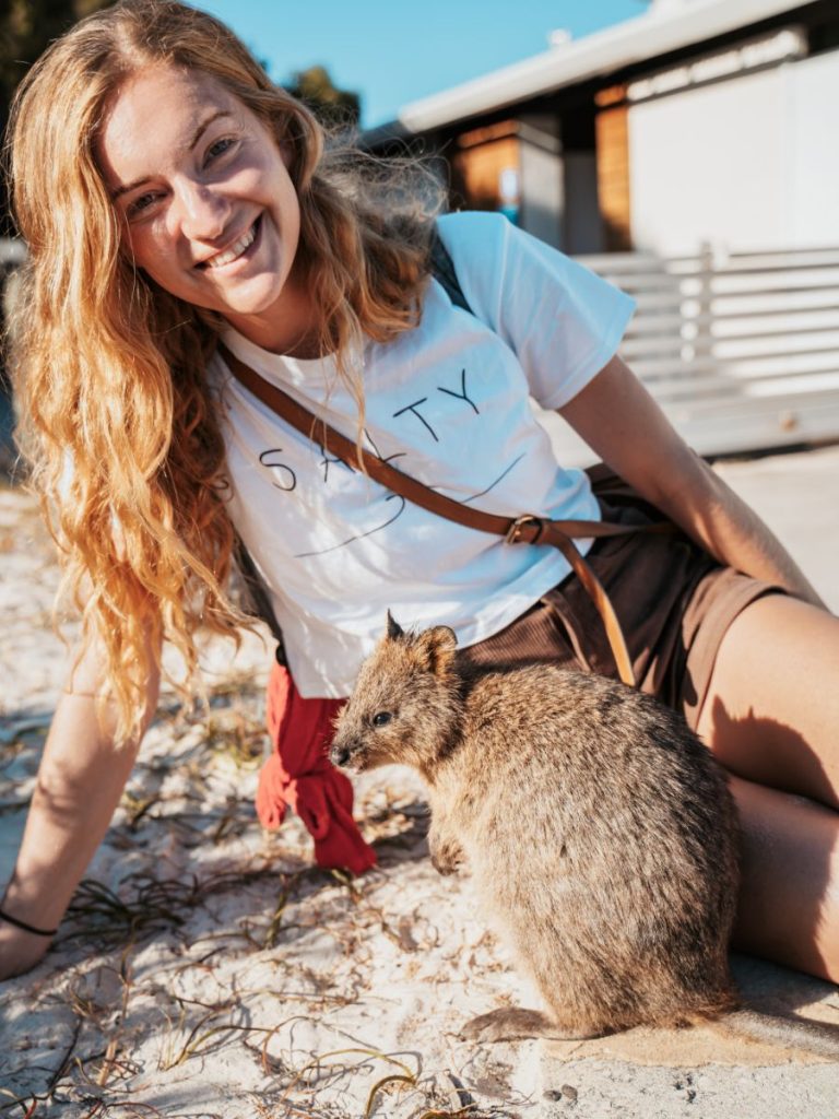 Beck of Salt and Charcoal kneels on the sandy ground of Rottnest Island next to a quokka.