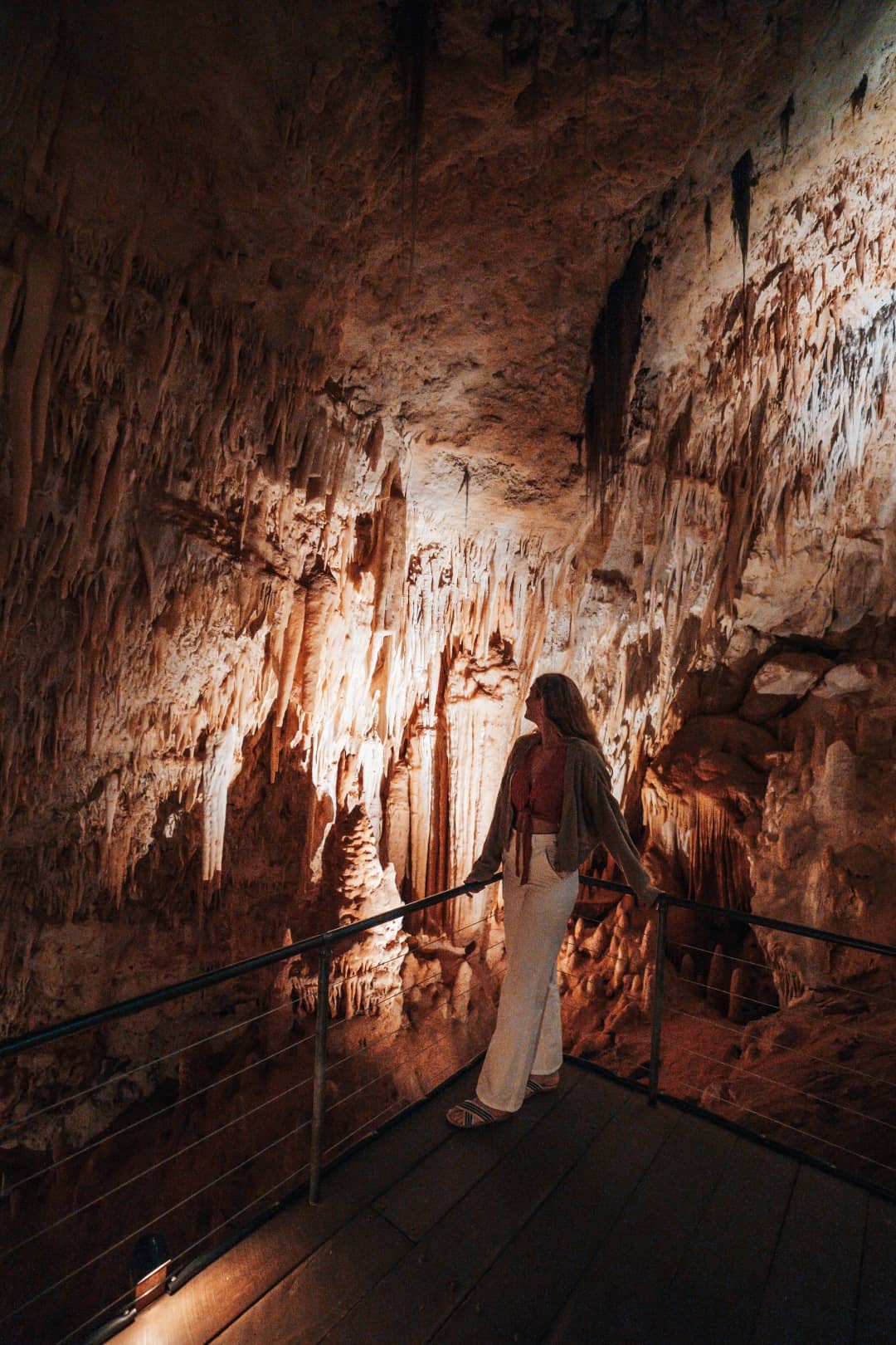 A woman stands on a wooden platform, looking out over the breathtaking view of an underground cave showing things to do in Margaret River, Western Australia