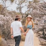 Chris and Beck of Salt and Charcoal holding hands on a bushland path surrounded by lush Western Australia Wildflowers.