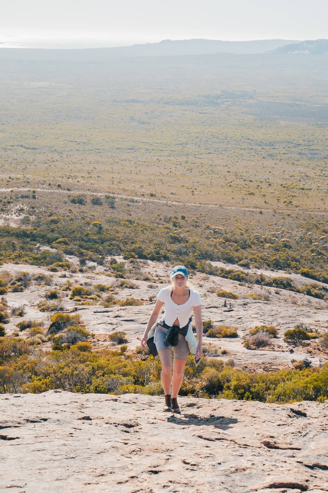 Beck of Salt and Charcoal hiking Frenchman Peak in Western Australia, with the expansive bushland stretching out behind her under a clear sky.