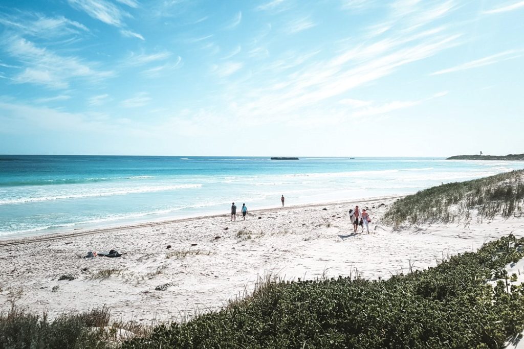 A few people walk along the white sandy beach of Lancelin, Western Australia, under a bright blue sky.