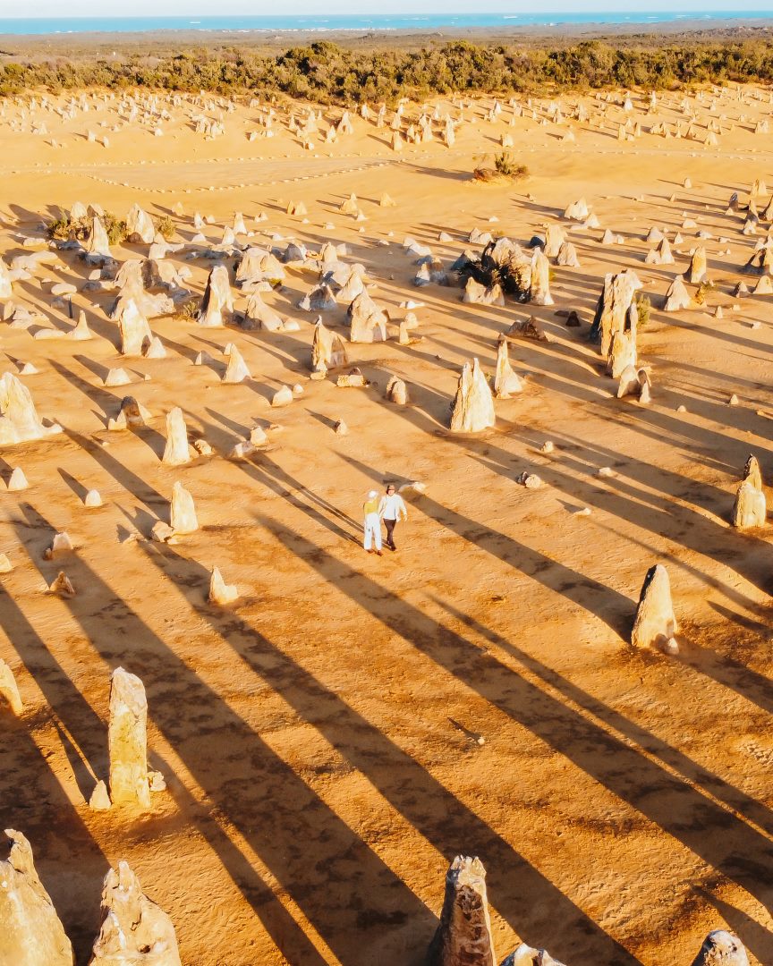 An aerial view of two people walking among the limestone formations of The Pinnacles Desert in Nambung National Park, Western Australia.