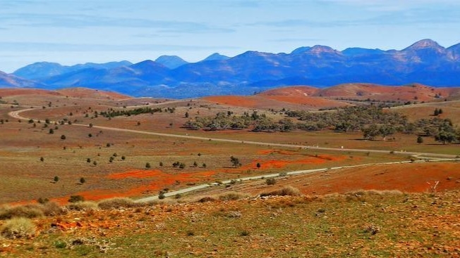 A sweeping view from Hucks Lookout showcases the rolling, red-tinged hills of the Flinders Ranges with rugged mountains in the distance, a highlight of a Flinders Ranges itinerary.