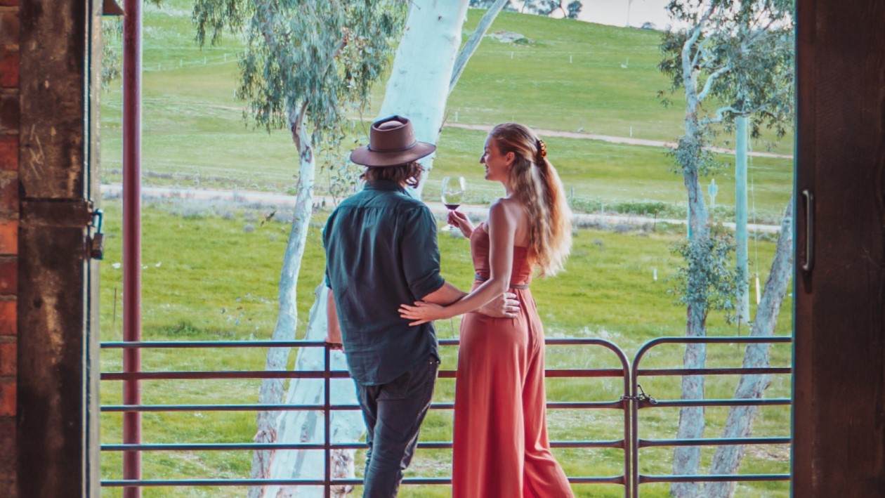 Chris and Bec on balcony overlooking a green landscape, sharing a glass of wine.