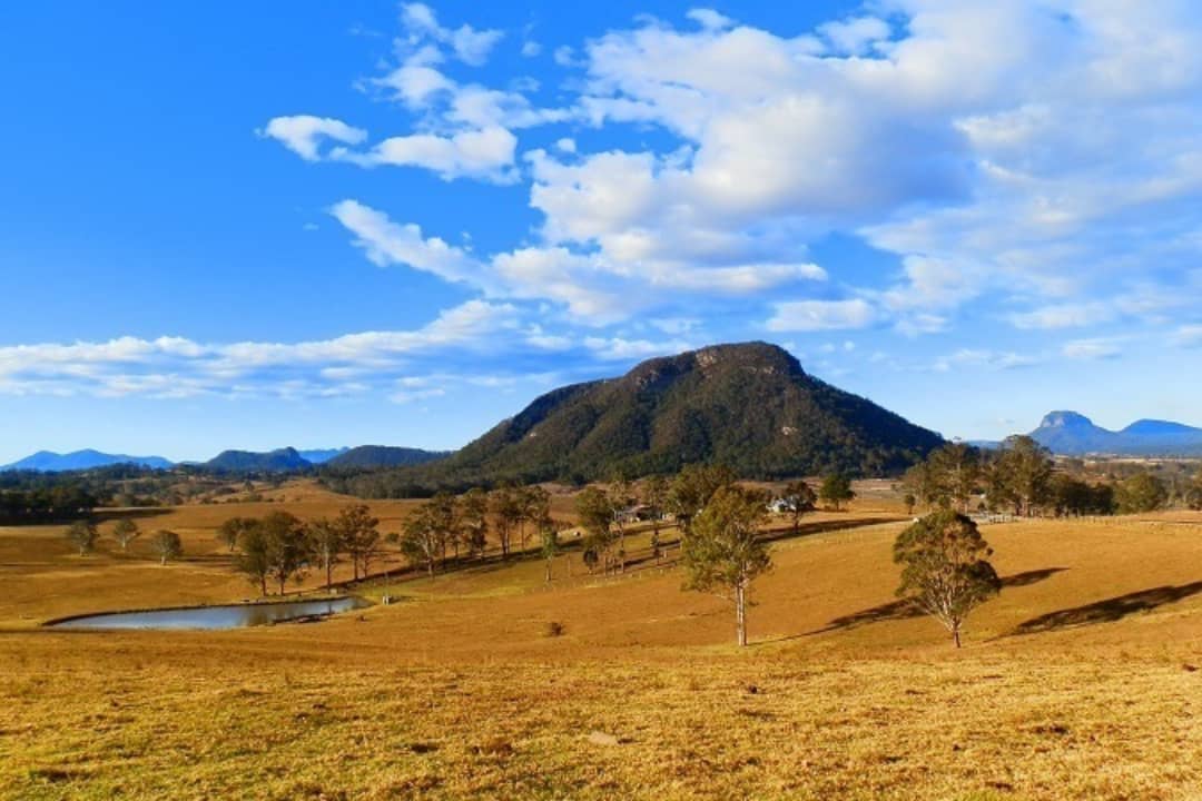 Rolling hills and a scenic mountain view in Woodenbong, New South Wales, with a clear blue sky and scattered clouds.