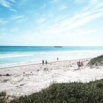 A peaceful white sandy beach with clear blue water and a group of people walking along the shore at Lancelin.