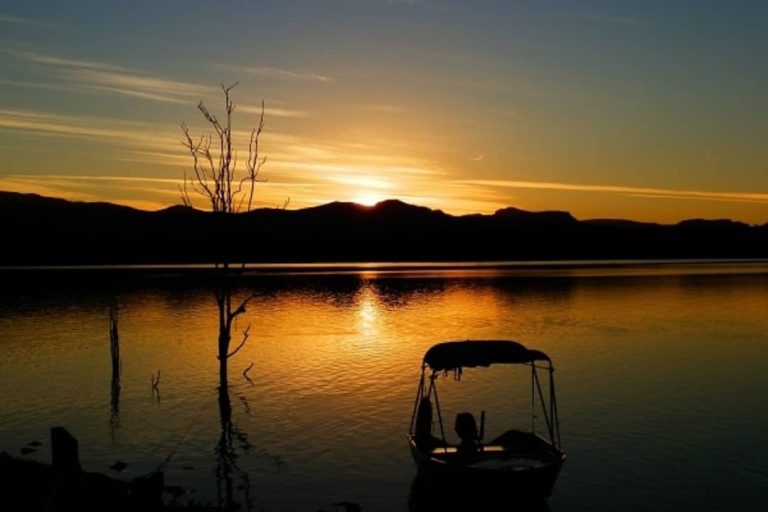 Silhouette of a small boat at sunset on Lake Moogerah, with calm waters and a mountainous horizon in Scenic Rim.