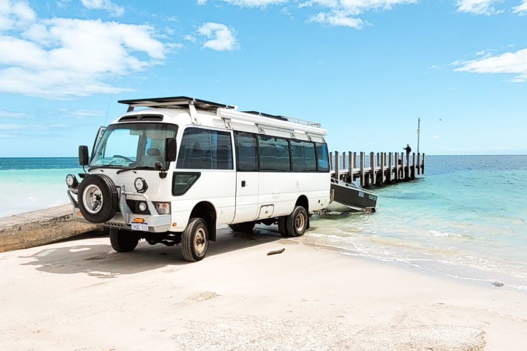 A rugged, white vehicle with a boat trailer is parked on the beach near Busselton Jettyโs boat ramp, set against the backdrop of turquoise waters. This image reflects the jetty's accessibility for boating and marine activities in Western Australia.