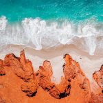 Aerial view of Cape Leveque on the Dampier Peninsula near Broome, showcasing vibrant red cliffs, white sandy beach, and turquoise ocean waves crashing onto the shore.