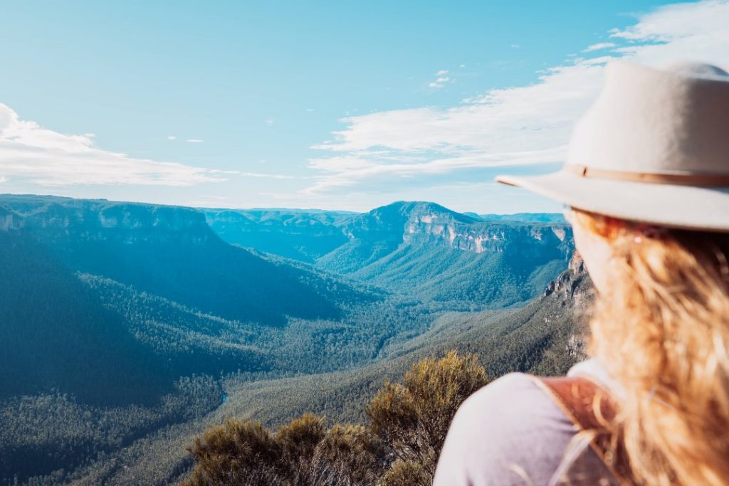 A hiker enjoying the serene views on a trail leading to Fortress Falls in the Blue Mountains, a destination known for the best Blue Mountains tours. The expansive valley and dense forest create a picturesque backdrop.