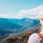 A hiker enjoying the serene views on a trail leading to Fortress Falls in the Blue Mountains, a destination known for the best Blue Mountains tours. The expansive valley and dense forest create a picturesque backdrop.