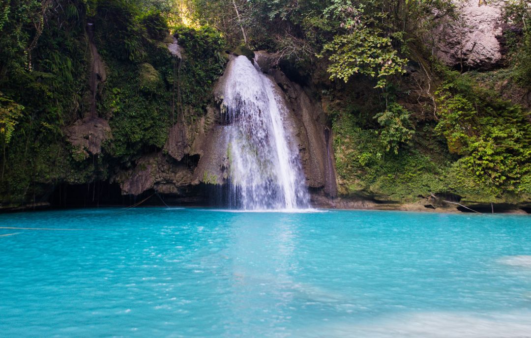 Turquoise water cascades from a lush jungle waterfall into a serene natural pool at Kawasan Falls, one of the top things to do in Cebu for nature lovers.
