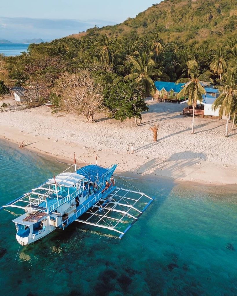 A traditional Filipino outrigger boat docked on a pristine beach with lush greenery in the background, highlighting the budget-friendly Philippines travel cost for island hopping.