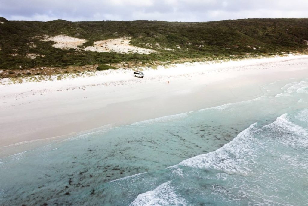 A wide aerial shot of Bremer Bay’s white sandy beach with a camper van parked by the dunes—perfect beachside camping on a Perth to Bremer Bay road trip.