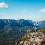 Hiker standing on a rocky outcrop at Lockleys Pylon, overlooking sweeping forested valleys and cliffs in the Blue Mountains, NSW.