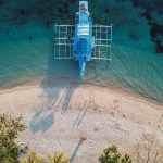 Aerial view of a blue bangka boat docked on a sandy beach between Coron and El Nido, a scenic stop during one of the top island-hopping things to do in the Philippines.