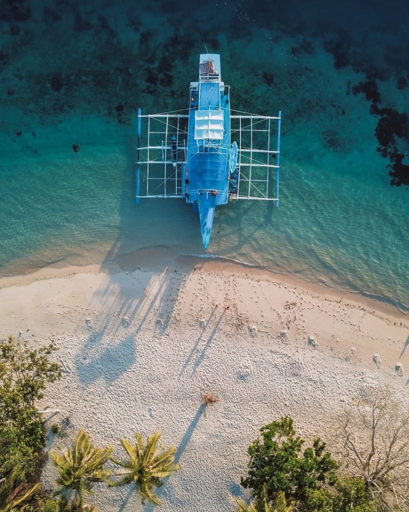 Aerial view of a blue bangka boat docked on a sandy beach between Coron and El Nido, a scenic stop during one of the top island-hopping things to do in the Philippines.