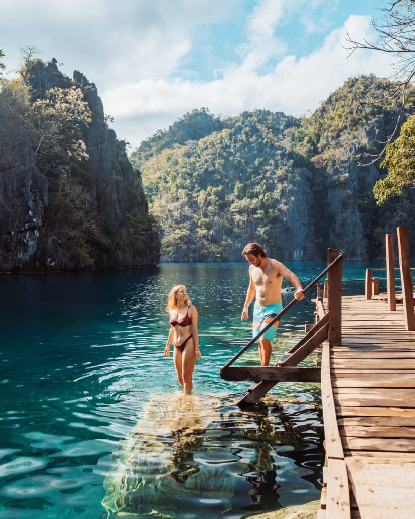 Couple stepping into the crystal-clear waters of Kayangan Lake, enjoying one of the most iconic things to do in Coron, Philippines.