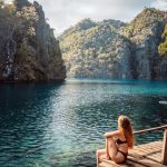 Woman sitting on a wooden deck by the turquoise waters of Kayangan Lake, one of the top things to do in Coron, Philippines.