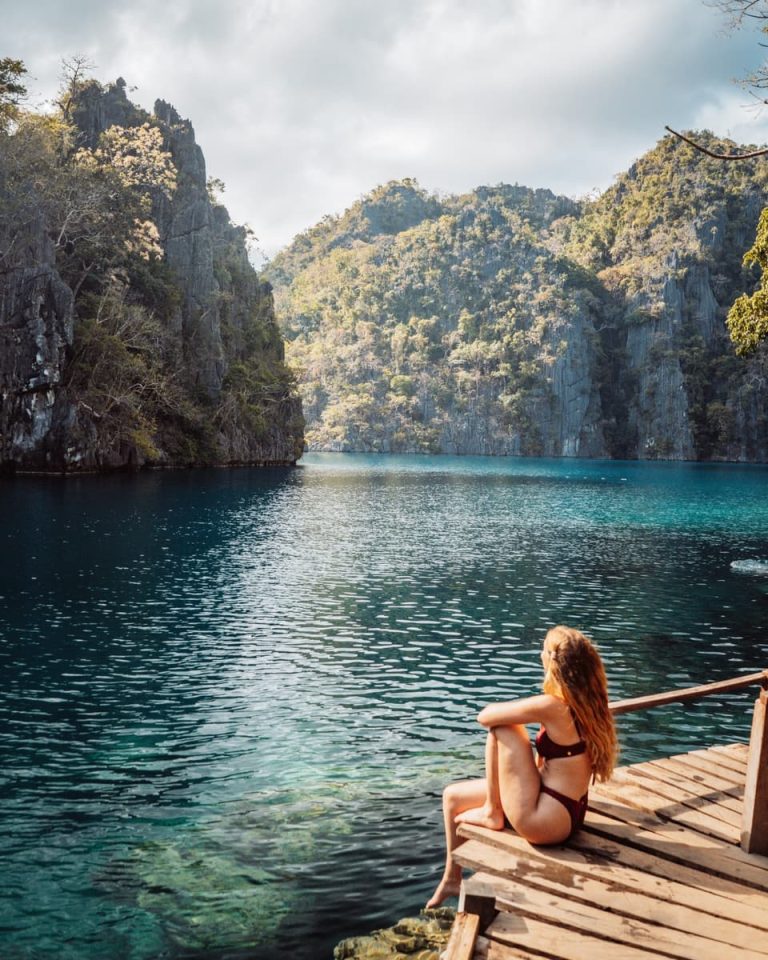 Woman sitting on a wooden deck by the turquoise waters of Kayangan Lake, one of the top things to do in Coron, Philippines.