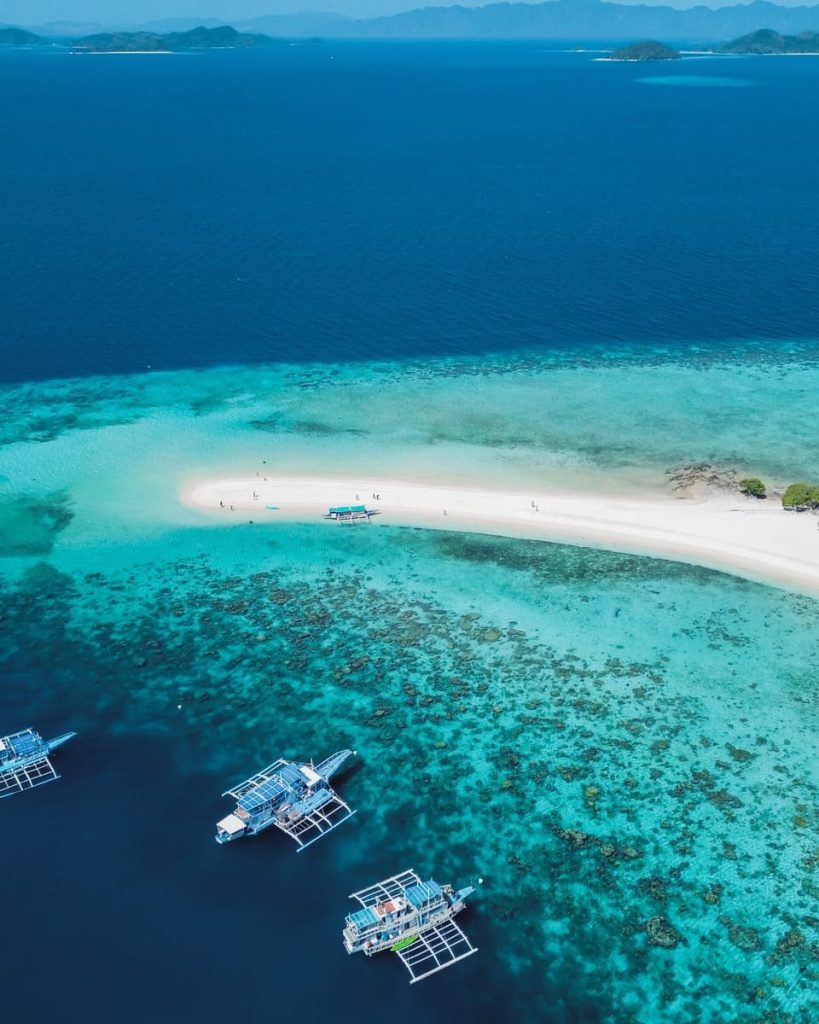 Aerial view of boats anchored near a white sandbar between Coron and El Nido during a Keeloma Island hopping tour, one of the most scenic things to do in the Philippines.