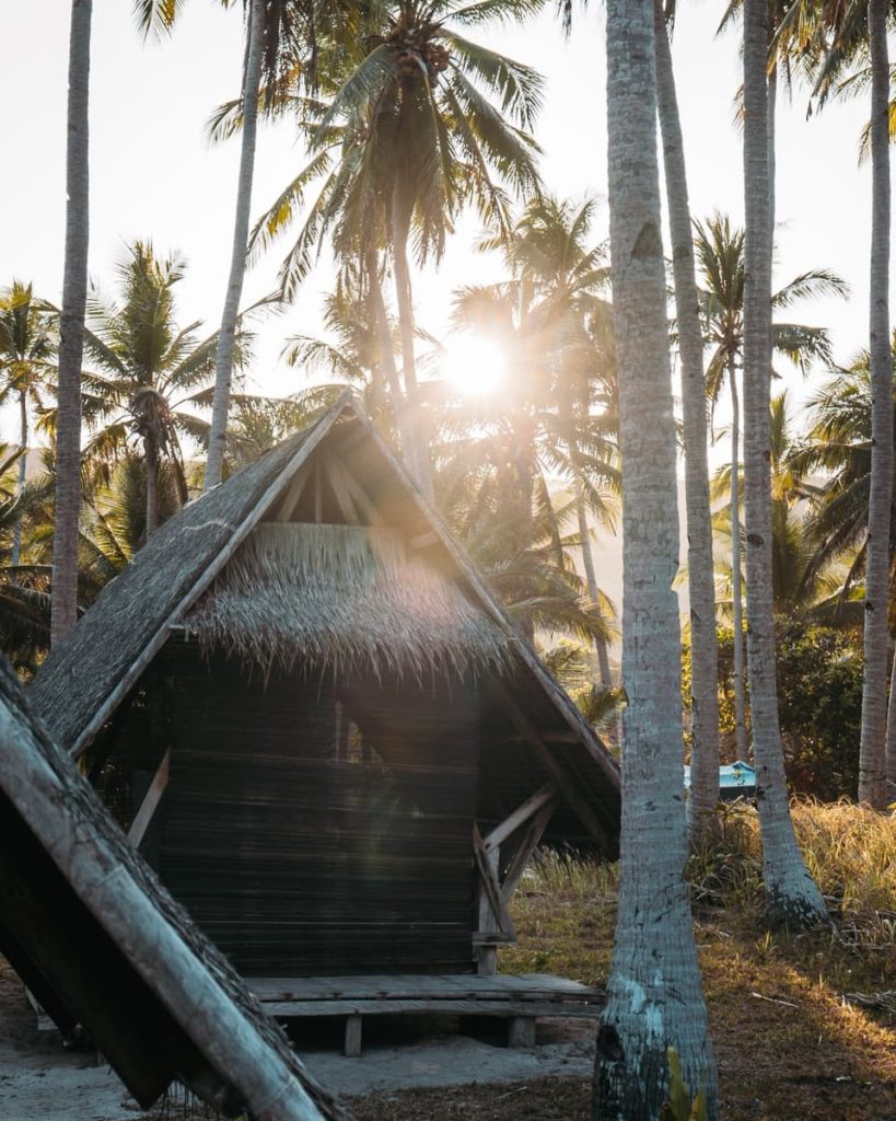 Rustic beach hut under palm trees during sunset on a Keeloma Island hopping tour, a peaceful option among the things to do in Coron, Philippines.