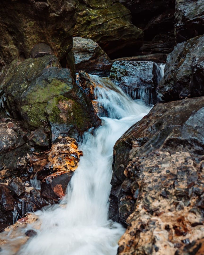 Fast-flowing water running between mossy rocks in a narrow channel, part of a hidden stream near the secret infinity pool Blue Mountains area.