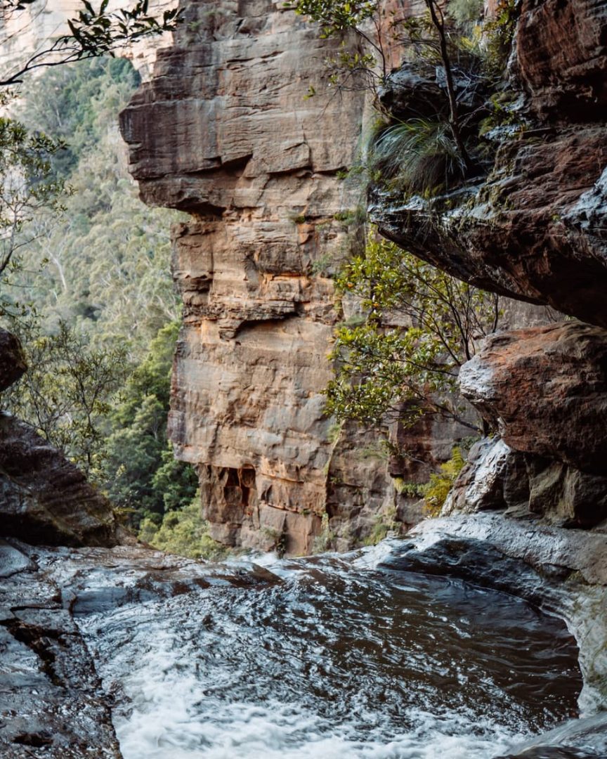 Top view of the secret infinity pool Blue Mountains, where water flows over the edge of a rock platform with towering sandstone cliffs in the background.